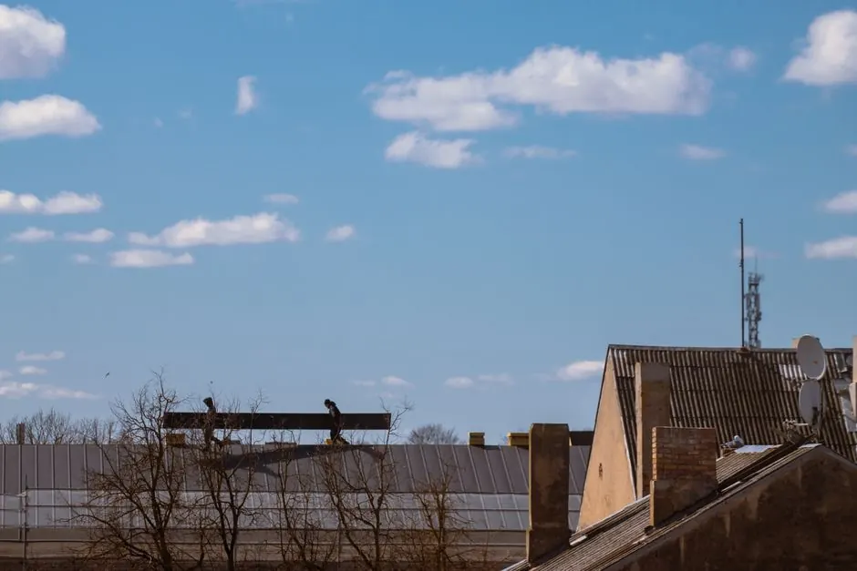 Silhouetted workers on a roof with clear blue sky and clouds in the background.